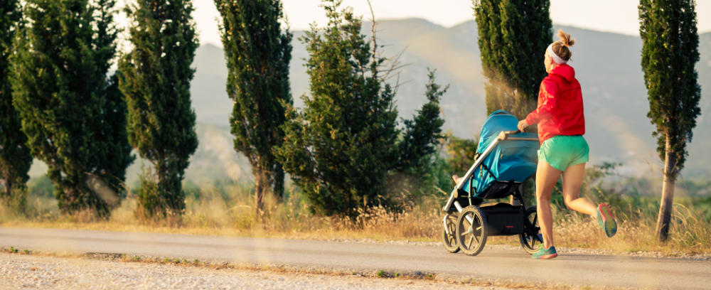 Joggen mit Kinderwagen: Frau joggt mit Stroller vor Pinien