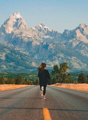 Illustration Workshop Joggen nach Geburt: Straße mit einer laufenden Frau im Fokus, am Horizont schneebedeckte Berge